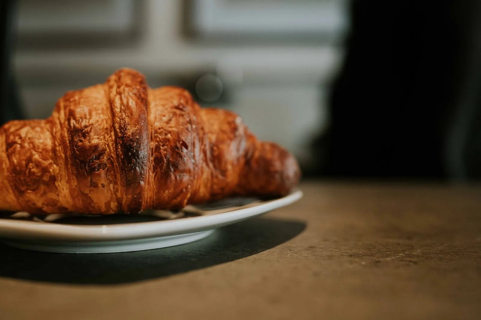 A delicious golden croissant displayed on a ceramic plate, perfect for breakfast settings.